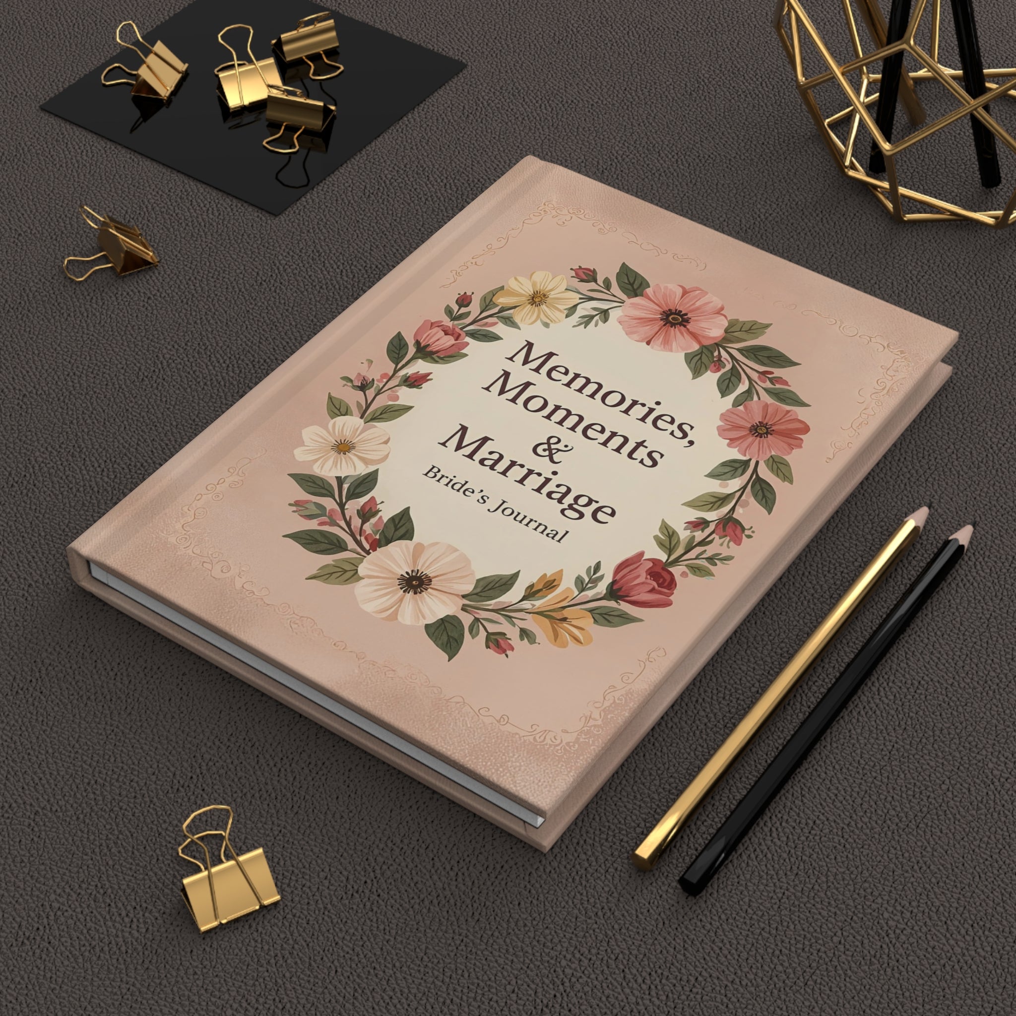 Journal titled 'Memories, Moments & Marriage' with floral design on a dark surface with stationery items.