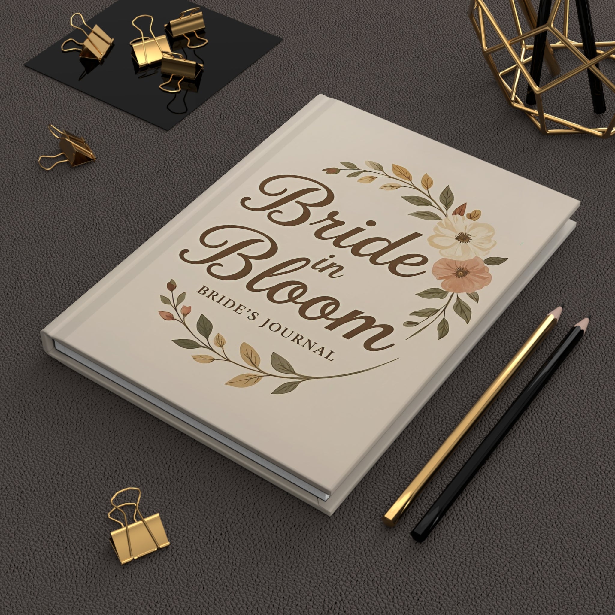 Book titled 'Bride in Bloom: Bride's Journal' on a dark surface with stationery items.