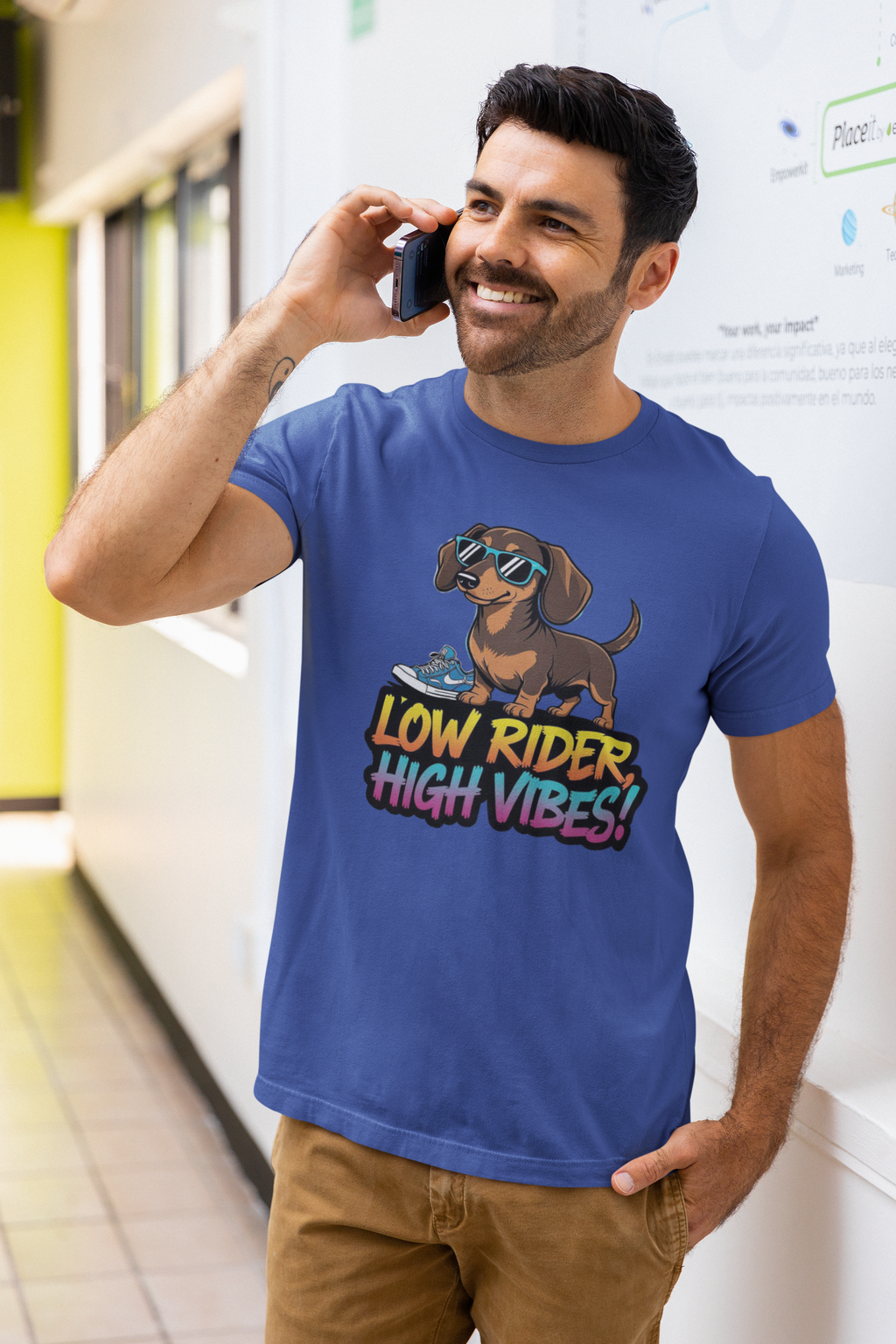 Man wearing a blue t-shirt with a dachshund graphic and text, standing in a subway station.