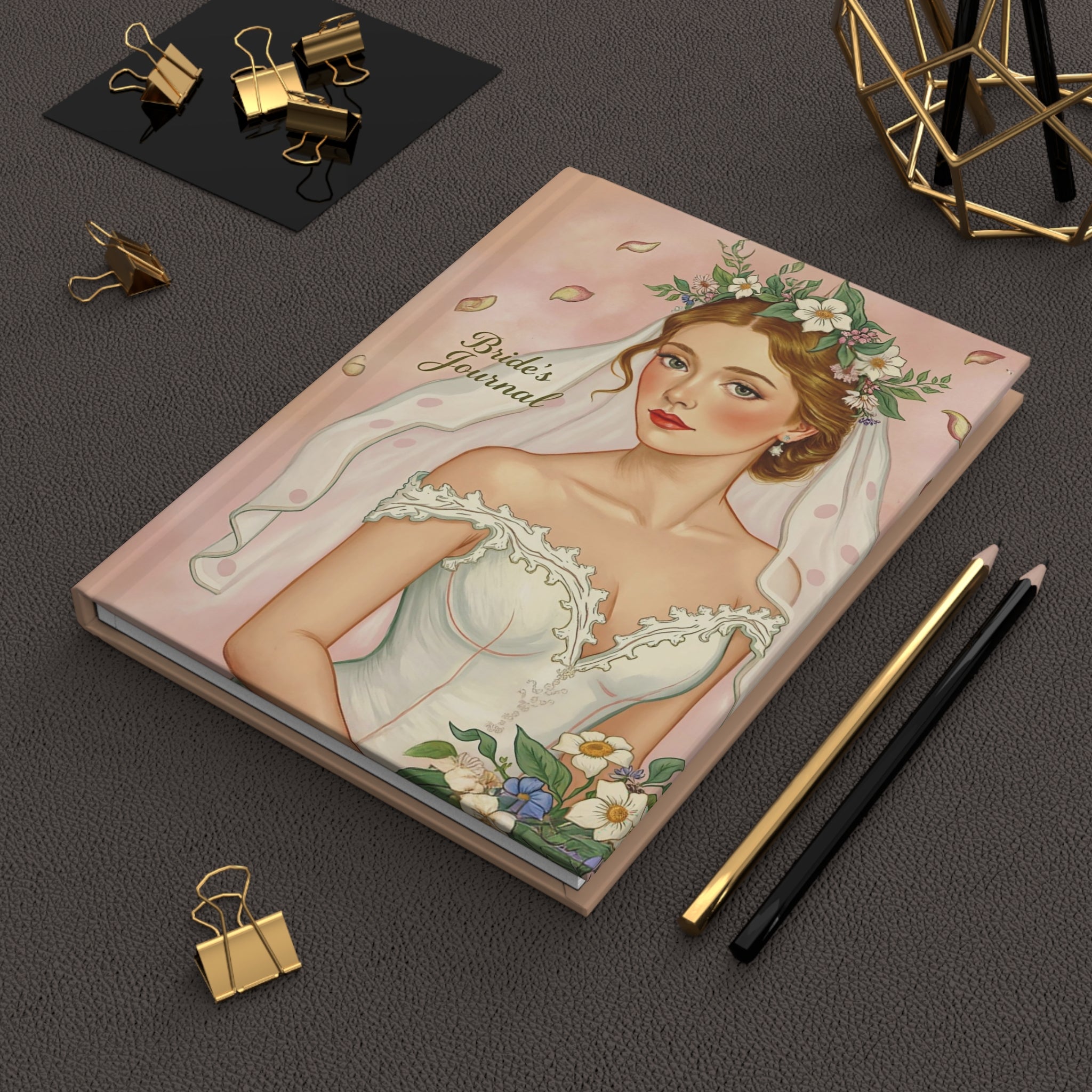 Notebook titled 'Bride's Journal' with a bride illustration on a dark surface with stationery items.